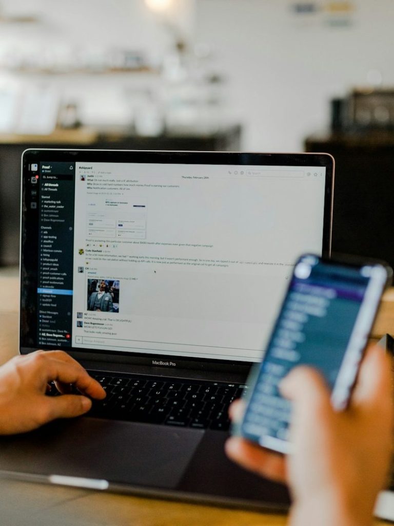 Person am Laptop mit Handy in der Hand Eine Person tippt auf einem Laptop und hält ein Smartphone in der Hand.